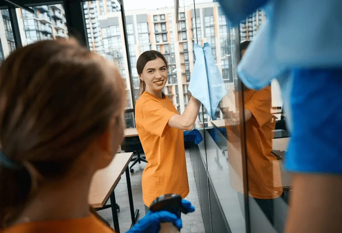 A cleaner spraying a piece of glass and wiping it to remove the fingerprints. 