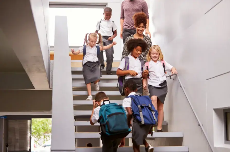 Primary school children walking up and down the stairs touching the bannisters, showing the importance of regularly cleaning touchpoints to prevent illness.